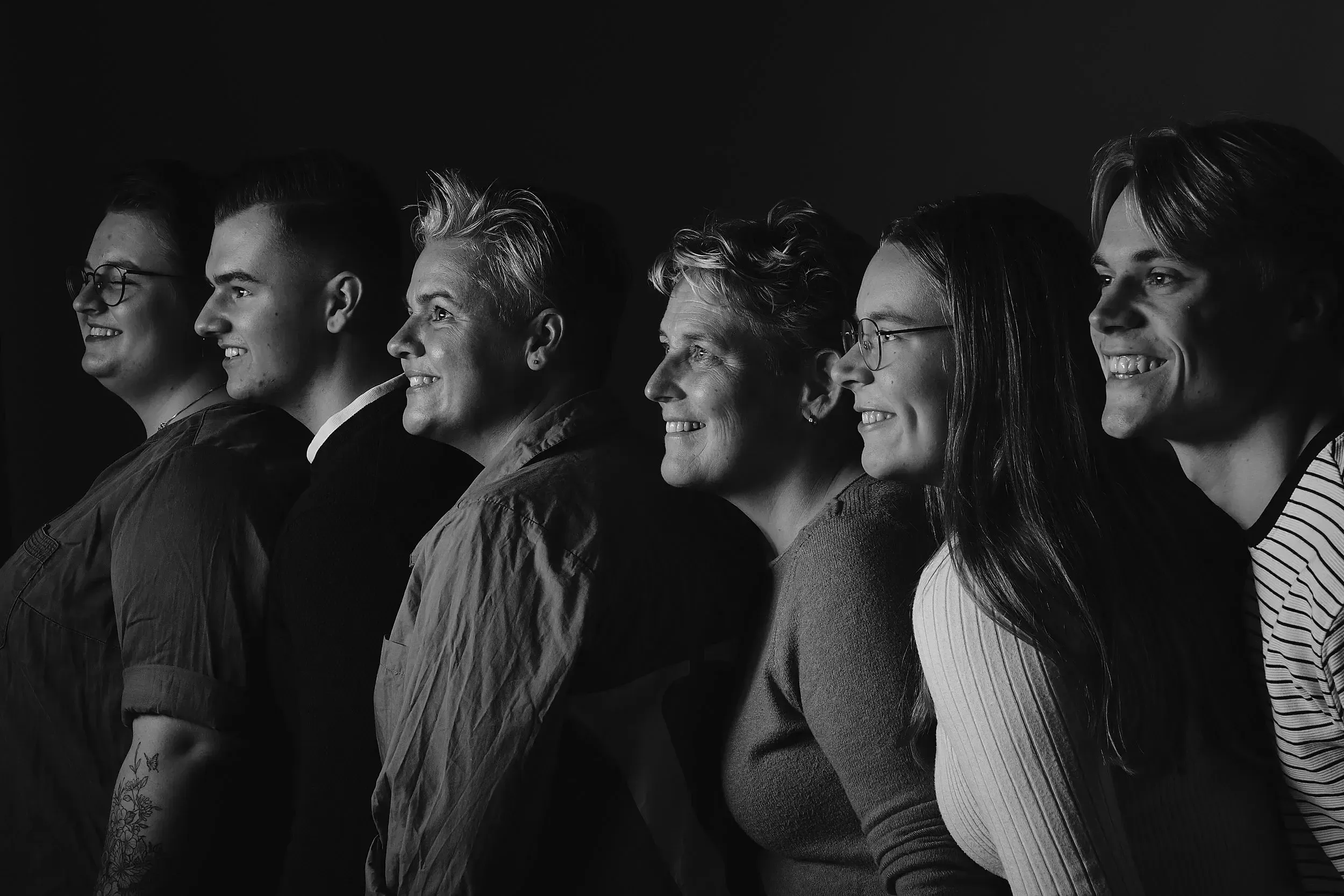 Groepsfoto met een elegante zwarte achtergrond en slechts één enkele lichtbron die een warme sfeer creëert.
