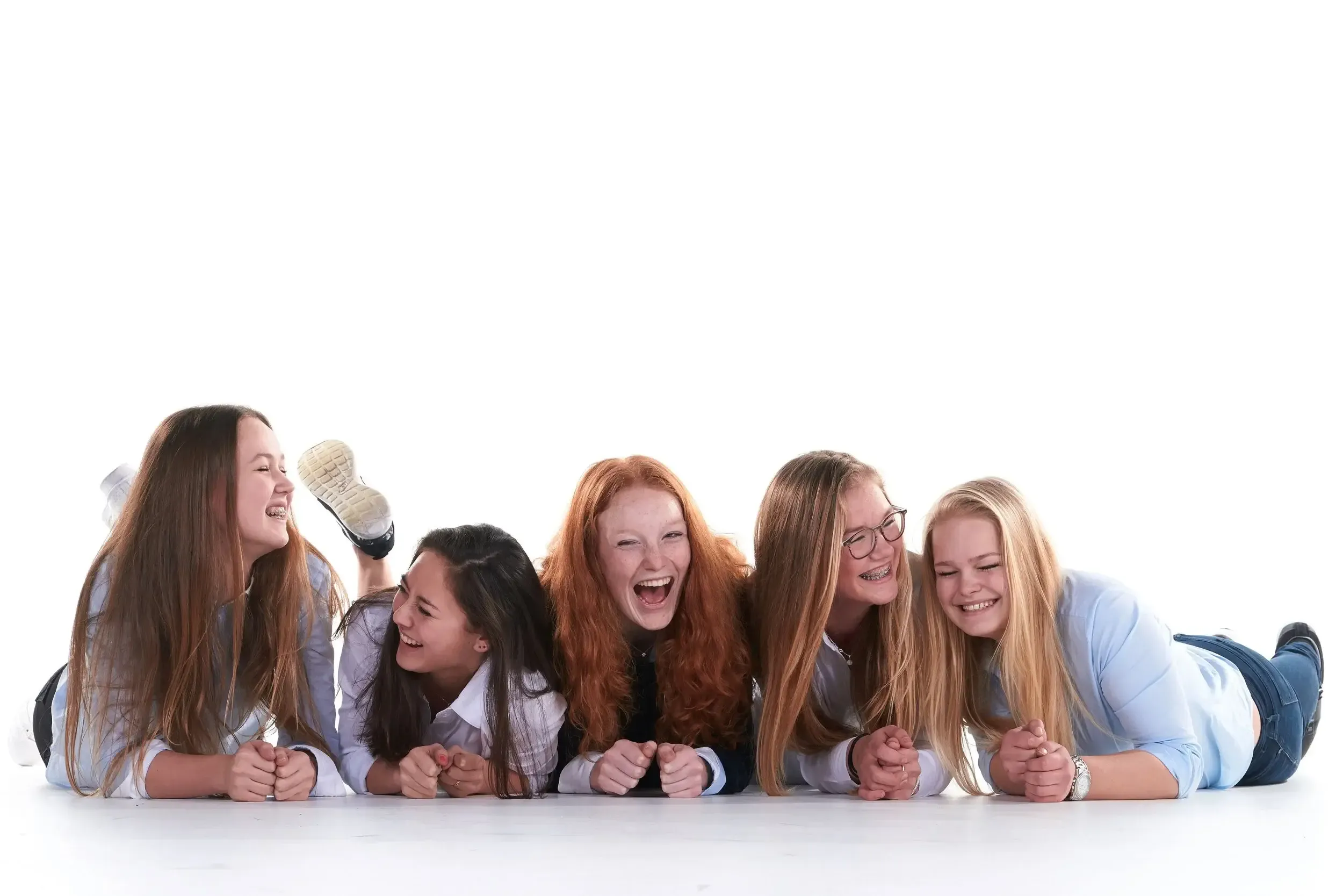 Vijf jonge vrouwen liggen op de buik op een witte achtergrond, lachen en praten samen.